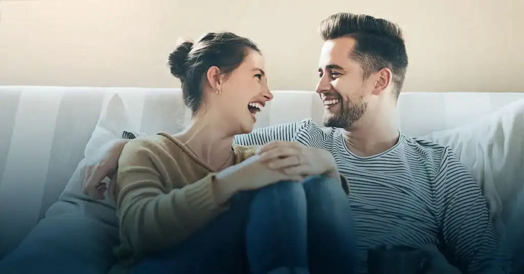 Smiling couple sitting close together on a couch, laughing and gazing at each other