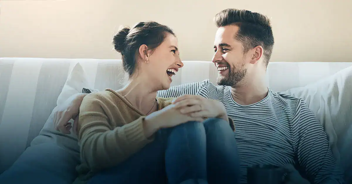 Smiling couple sitting close together on a couch, laughing and gazing at each other